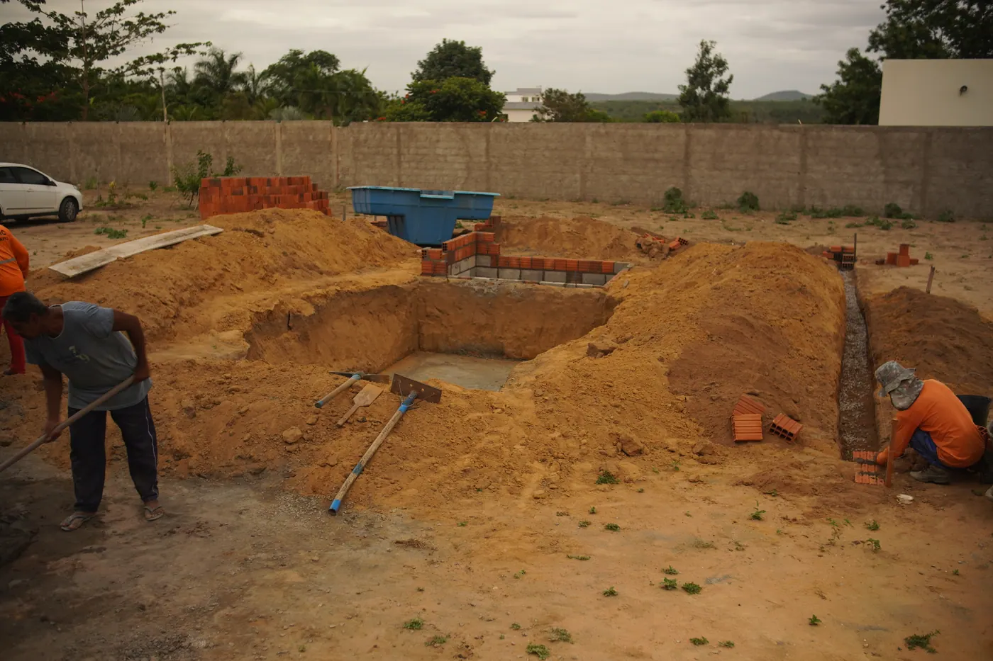 Terreno escavado para a piscina, com alvenaria de apoio sendo levantada